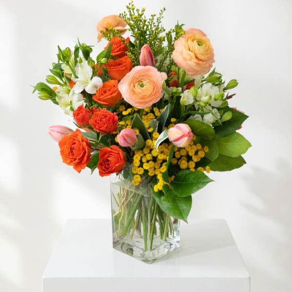 Mixed bouquet of orange and peach flowers in a clear glass vase