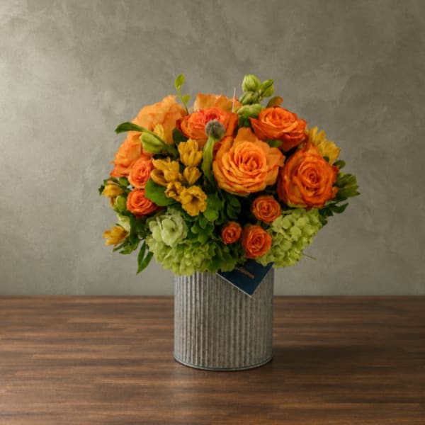 Orange roses and yellow flowers arranged in a ribbed metal vase