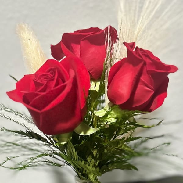 Three red roses with greenery and feathery accents