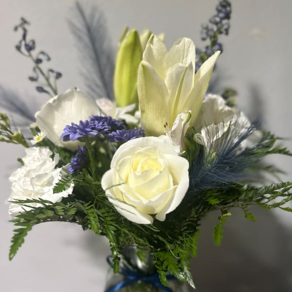 White roses and lilies arranged with purple flowers in a glass vase
