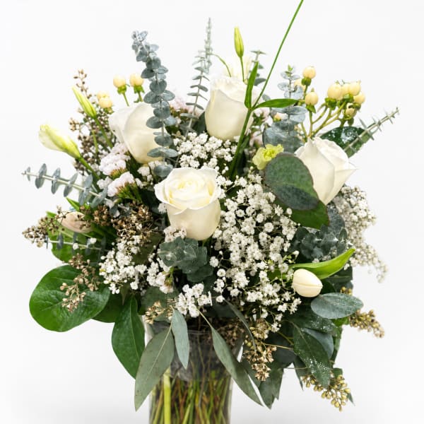 White roses and small white filler flowers in a glass vase