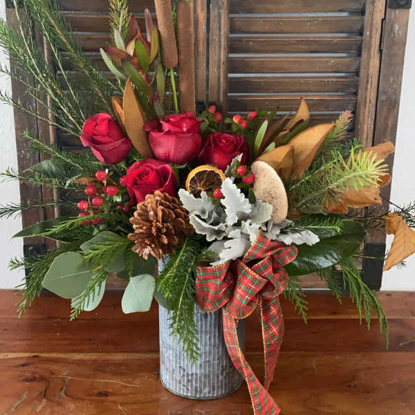 Red roses in a metal vase with pine, pinecones, and a plaid ribbon