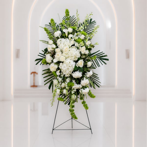 White floral standing spray with green accents on a black easel
