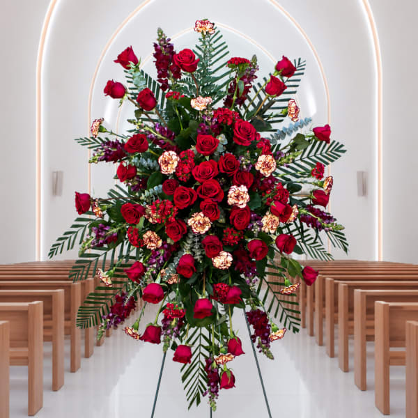 Large standing floral spray with red roses and purple accents in a church aisle