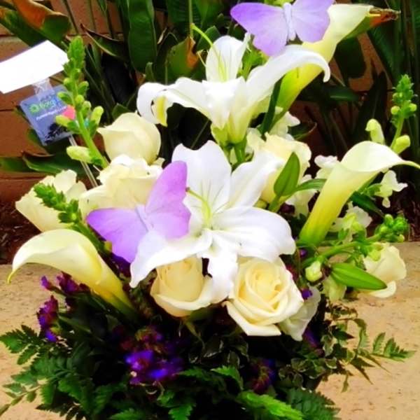 Bouquet of white lilies, cream roses, and purple butterflies in a purple wrap