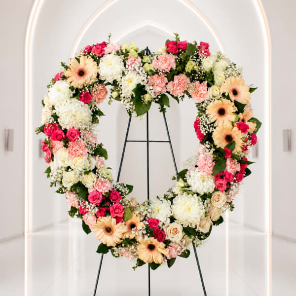 Heart-shaped floral wreath on a metal stand with pink, white, and peach blooms