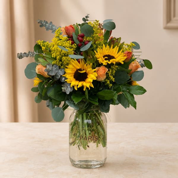 Bouquet of sunflowers and peach roses in a glass jar vase