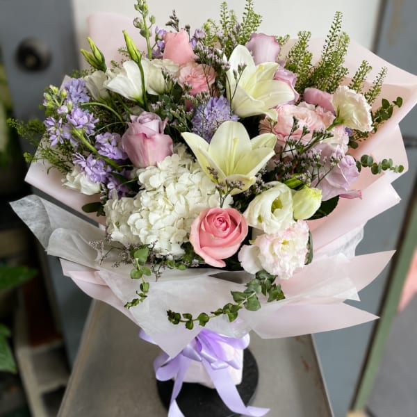 Pastel bouquet with pink roses, white lilies, and lavender flowers wrapped in pale paper