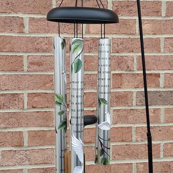 Black metal wind chime with silver tubes and bird designs hanging on a brick wall.