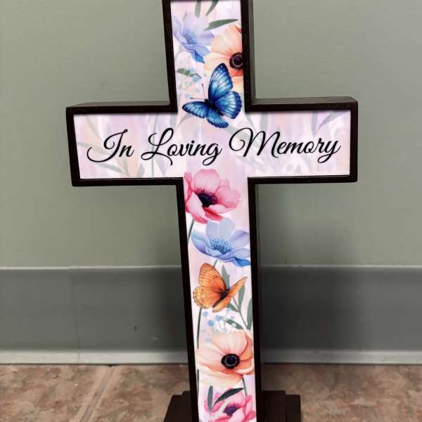 Cross-shaped memorial sign with floral and butterfly artwork and the words In Loving Memory