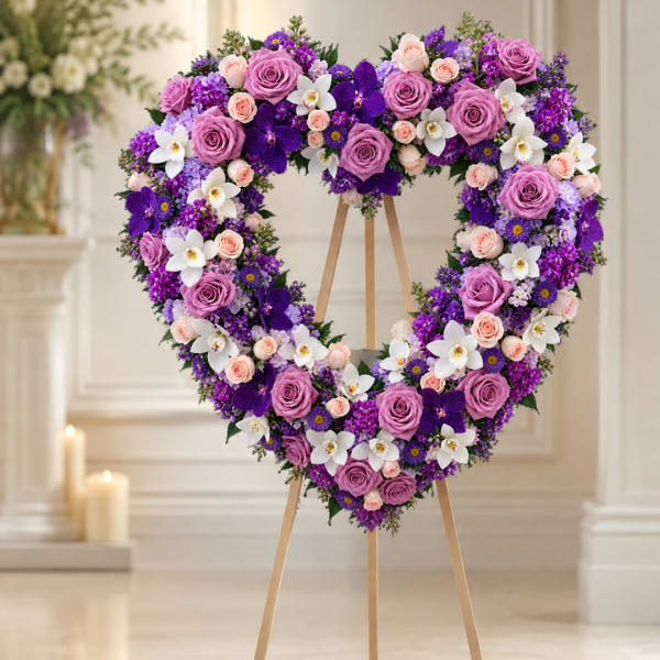 Heart-shaped floral wreath with purple, pink, and white flowers on a wooden stand