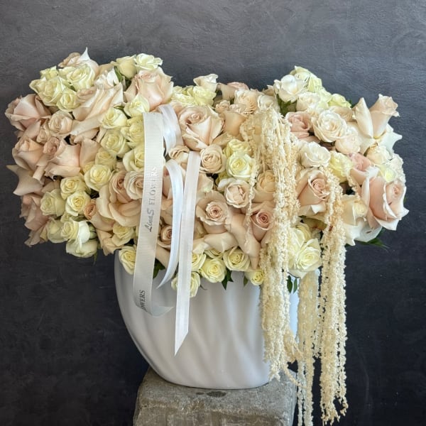 Large cream and blush rose arrangement in a white vase with trailing dried accents