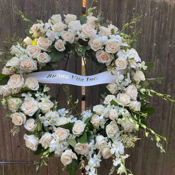 White rose wreath with orchids and a ribbon on a stand
