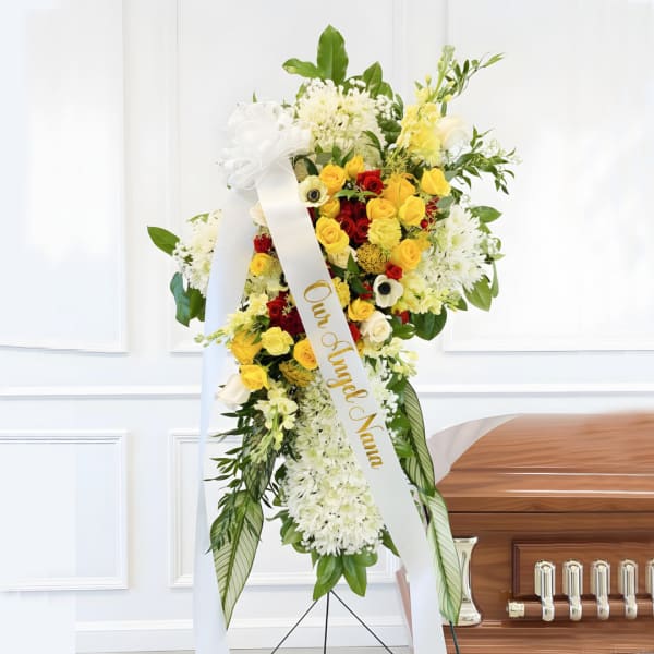 Standing funeral spray with yellow, red, and white flowers on a ribboned easel