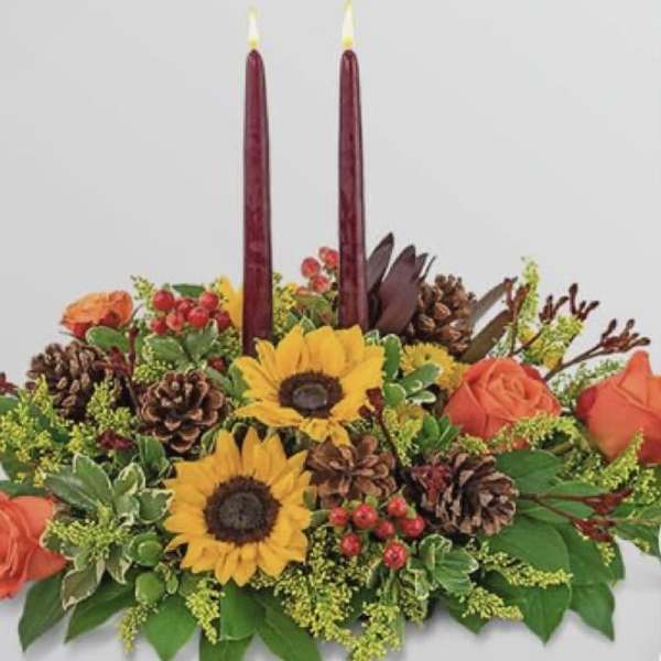 Autumn floral centerpiece with sunflowers, roses, pinecones, and two burgundy candles