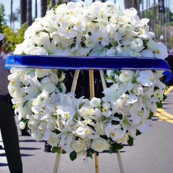 White floral funeral wreath on an easel with a blue ribbon