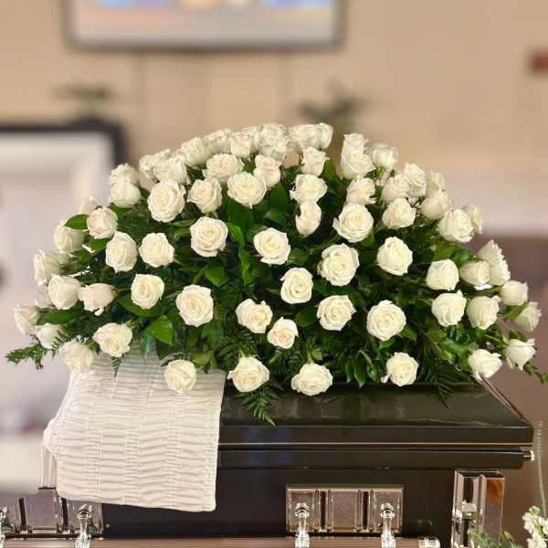 White rose arrangement on a dark casket with a white cloth drape