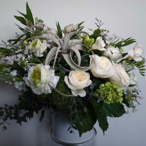 White floral arrangement in a vase with green accents and curled ribbon loops