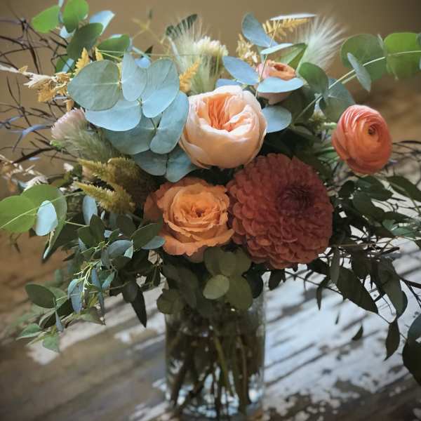 Peach and coral bouquet in a glass vase with blue-green foliage