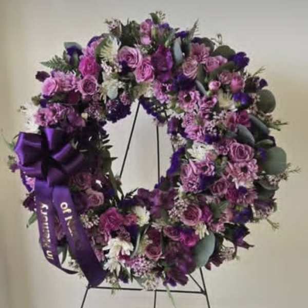 Purple floral wreath on a black stand with a ribbon bow
