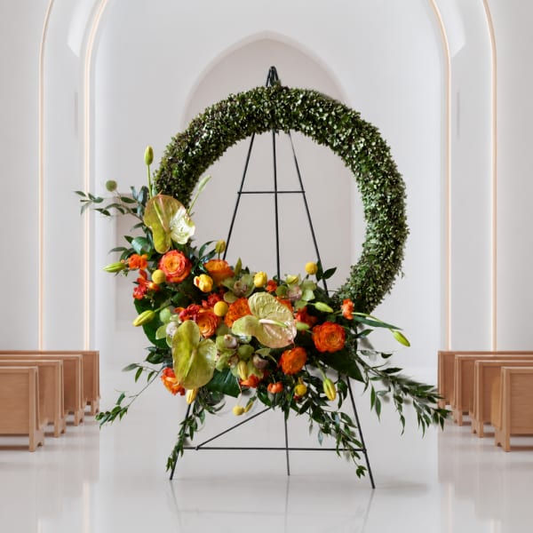 Floral wreath on a black stand with orange and yellow blooms