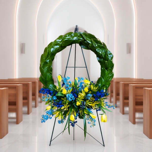 Large floral wreath on a stand with blue and yellow flowers in a church aisle