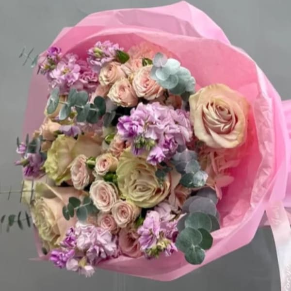 Bouquet of pale roses and purple flowers wrapped in pink paper