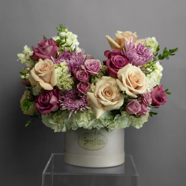 Bouquet of cream, pink, and purple flowers in a white hatbox