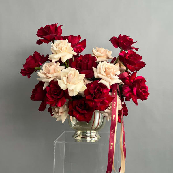 Red and cream roses arranged in a silver vase with a Dior ribbon