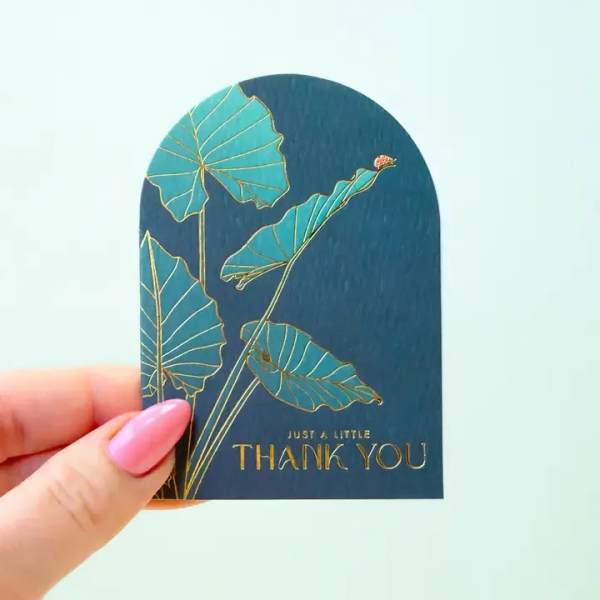 Hand holding a thank-you card with teal leaf artwork
