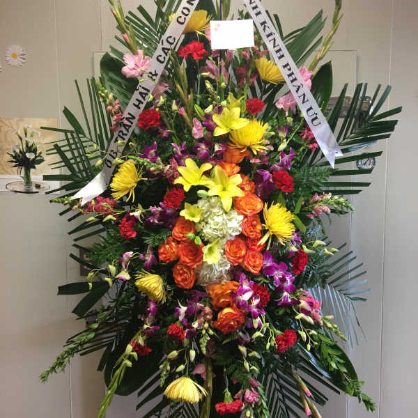 Large standing floral spray with colorful mixed blooms and white ribbons