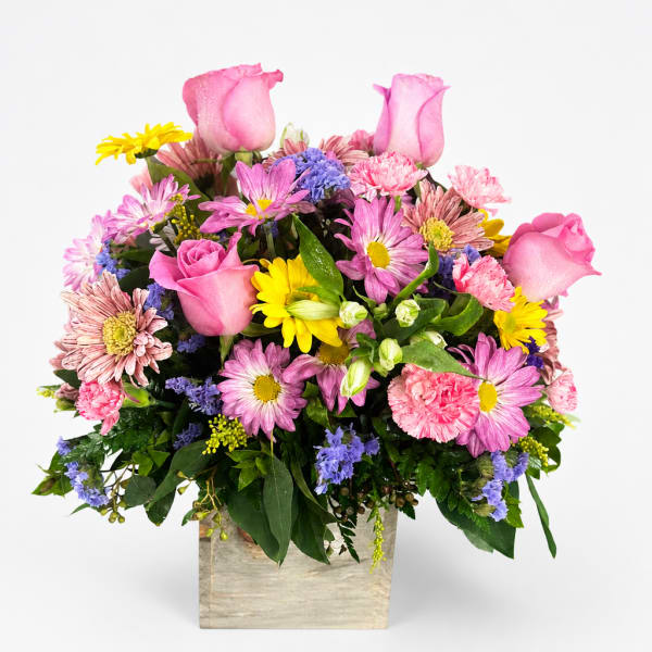 Mixed pink and yellow flowers arranged in a square wooden container