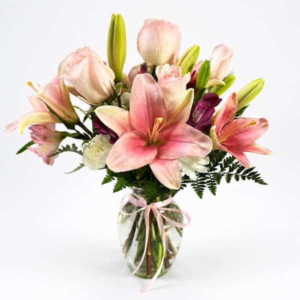 Pink lilies and roses in a glass vase with a ribbon