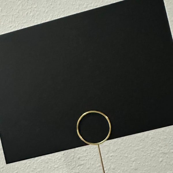 Black card with a gold ring pick on a textured surface