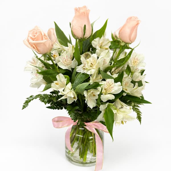 Peach roses and white alstroemeria in a glass vase with a pink ribbon