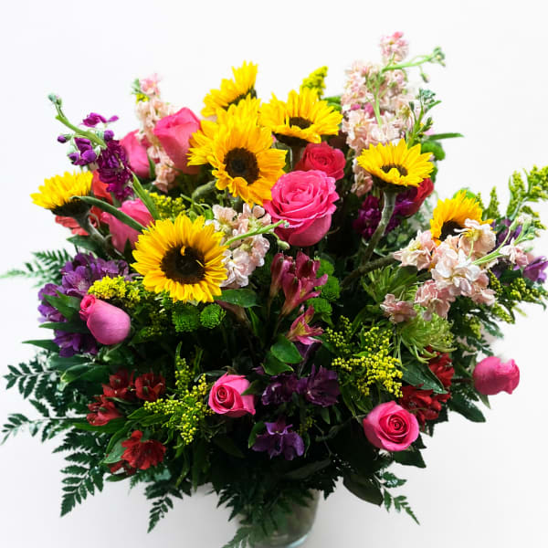 Mixed bouquet with sunflowers, pink roses, and purple flowers in a glass vase