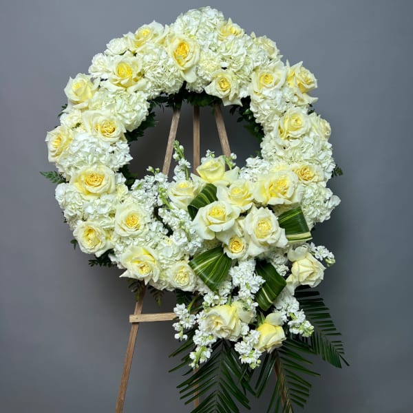 White and pale yellow floral funeral wreath on a wooden easel