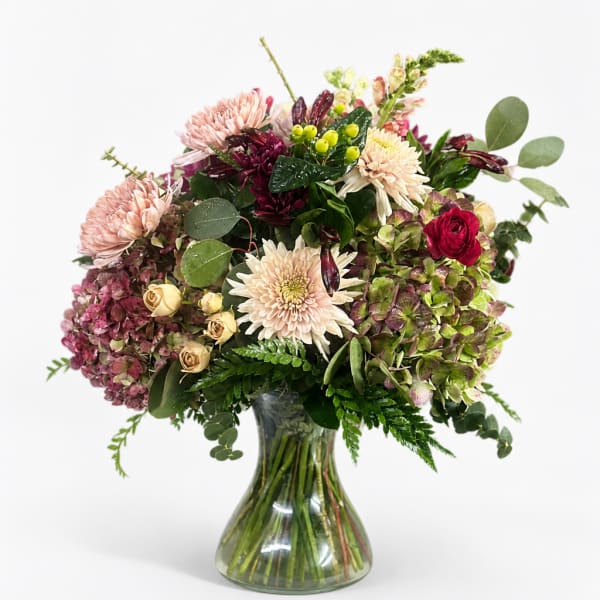 Mixed bouquet of pink, cream, and burgundy flowers in a clear glass vase