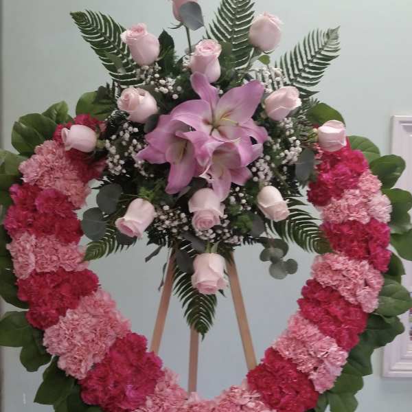 Heart-shaped floral wreath with pink roses and lilies on an easel