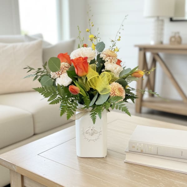 Orange and white flower arrangement in a white vase on a coffee table