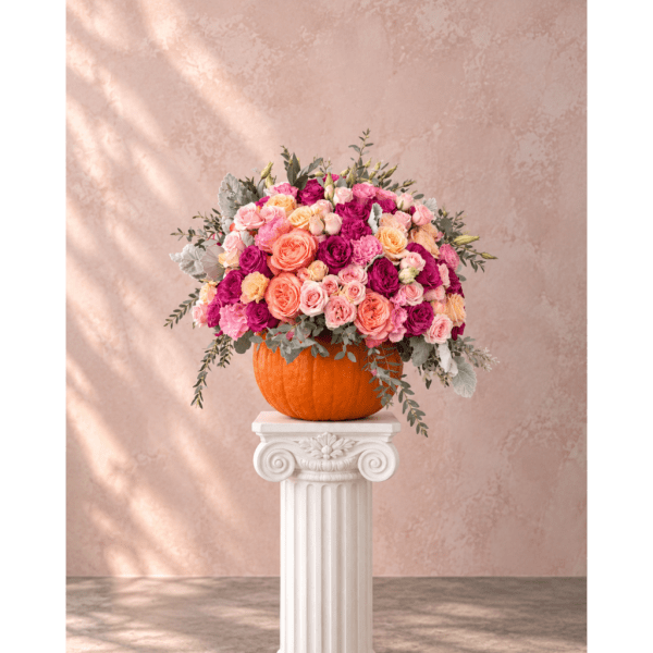 Pink and peach rose arrangement in a pumpkin vase on a white pedestal