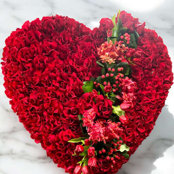 Heart-shaped red rose arrangement with pink flowers and greenery