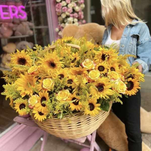 Large basket of yellow sunflowers and roses being held by a woman