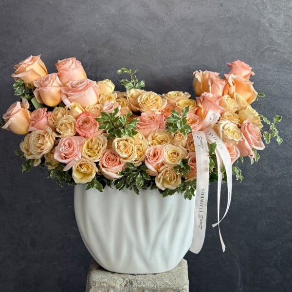 Peach and blush roses arranged in a white vase with ribbon accents