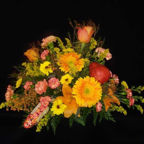 Colorful floral arrangement with yellow and orange blooms and a red apple