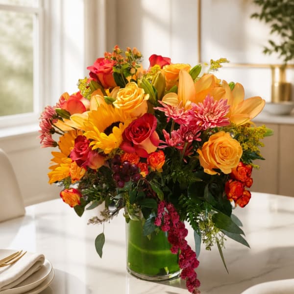 Mixed bouquet of roses, lilies, and sunflowers in a glass vase