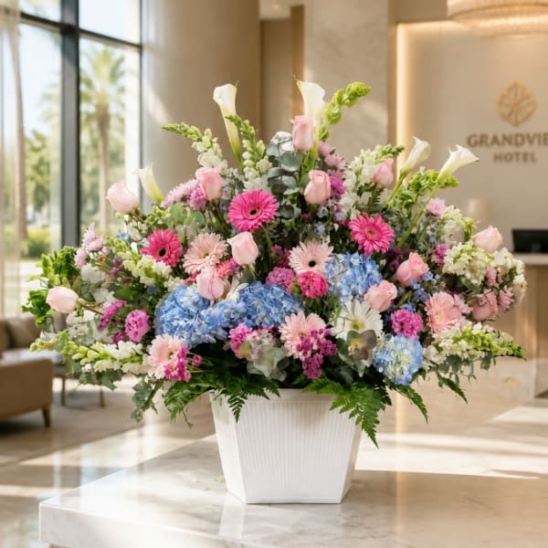 Large mixed flower arrangement in a white vase with pink, blue, and white blooms