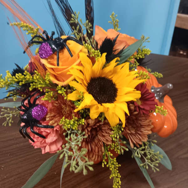 Autumn floral arrangement with sunflowers, roses, and Halloween spider decorations in a pumpkin container