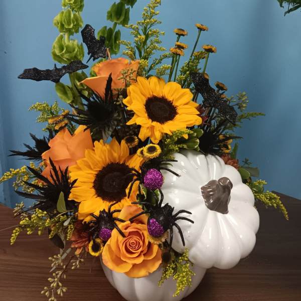 Orange and yellow floral arrangement in a white pumpkin container with black spider decorations