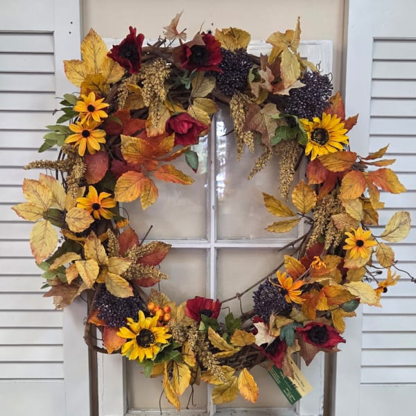 Fall wreath with sunflowers, red flowers, and autumn leaves on a window
